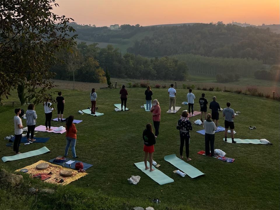 Gruppo di persone che pratica movimento all'aperto sui tappetini al tramonto